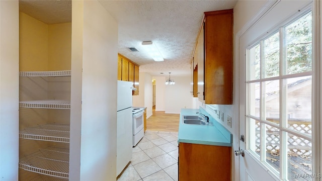 kitchen featuring white appliances, sink, a textured ceiling, decorative light fixtures, and light tile patterned floors