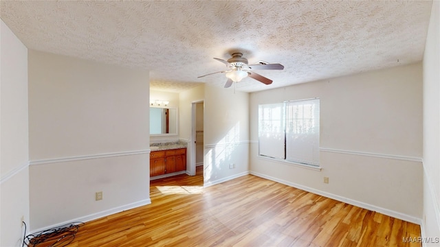 interior space with light hardwood / wood-style flooring, a textured ceiling, ensuite bathroom, and ceiling fan