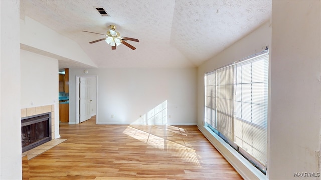 unfurnished living room featuring a tiled fireplace, ceiling fan, a textured ceiling, light wood-type flooring, and vaulted ceiling