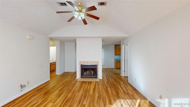 unfurnished living room with lofted ceiling, ceiling fan, a textured ceiling, a tile fireplace, and light hardwood / wood-style floors