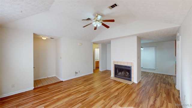 unfurnished living room featuring lofted ceiling, ceiling fan, a textured ceiling, light wood-type flooring, and a fireplace