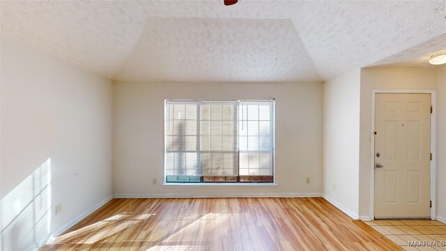 spare room featuring lofted ceiling, light hardwood / wood-style flooring, and a textured ceiling