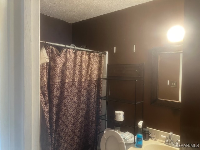 bathroom with a textured ceiling, sink, toilet, and curtained shower