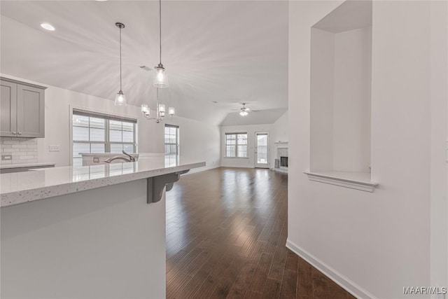 kitchen with ceiling fan with notable chandelier, pendant lighting, tasteful backsplash, dark hardwood / wood-style flooring, and light stone counters