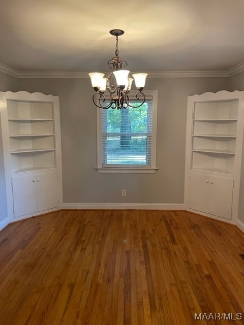 unfurnished dining area featuring wood-type flooring, crown molding, and a chandelier