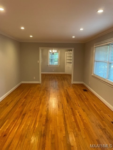 spare room featuring a notable chandelier, light wood-type flooring, and crown molding