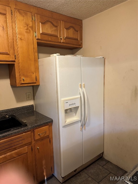 kitchen with dark tile patterned floors, sink, a textured ceiling, and white refrigerator with ice dispenser