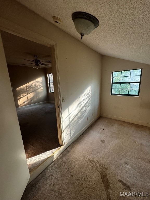 unfurnished room with ceiling fan, vaulted ceiling, carpet, and a textured ceiling