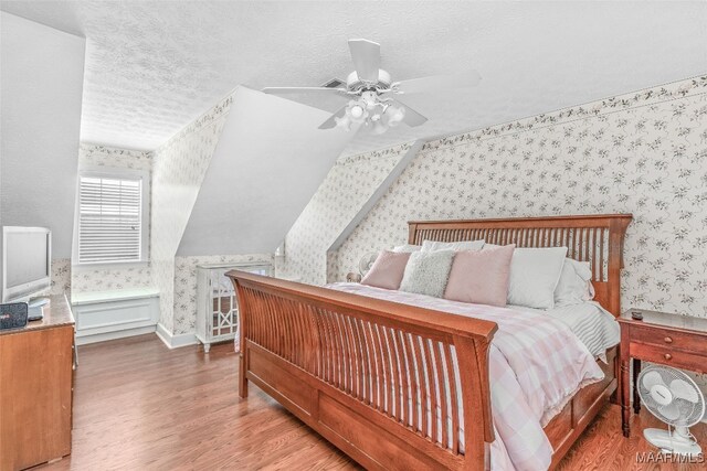 bedroom with ceiling fan, vaulted ceiling, wood-type flooring, and a textured ceiling