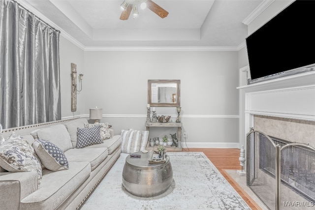 living room with a raised ceiling, ornamental molding, hardwood / wood-style flooring, and ceiling fan