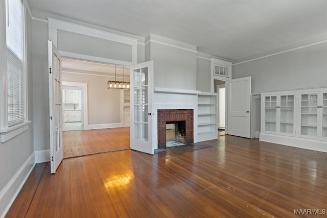 unfurnished living room featuring a brick fireplace, french doors, crown molding, and dark hardwood / wood-style flooring