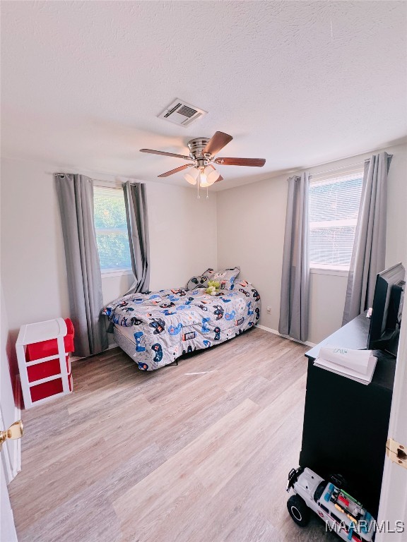 bedroom with a textured ceiling, multiple windows, ceiling fan, and light hardwood / wood-style flooring