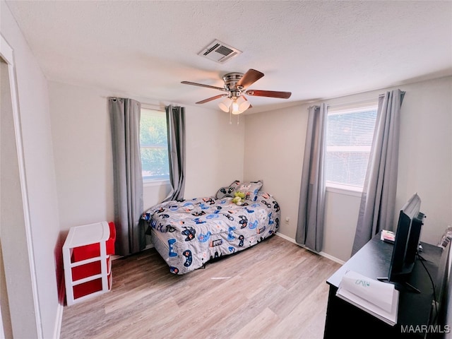 bedroom featuring a textured ceiling, light wood-type flooring, multiple windows, and ceiling fan