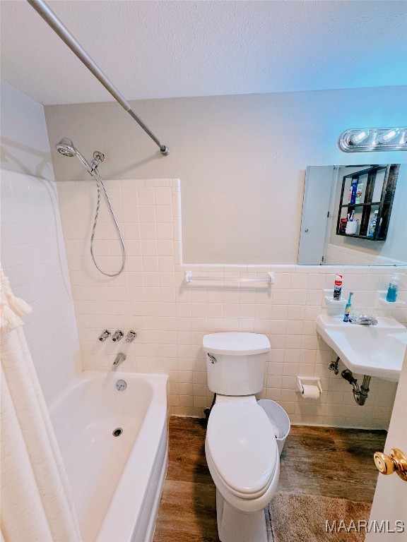 full bathroom with sink, wood-type flooring, shower / bath combo with shower curtain, tile walls, and toilet