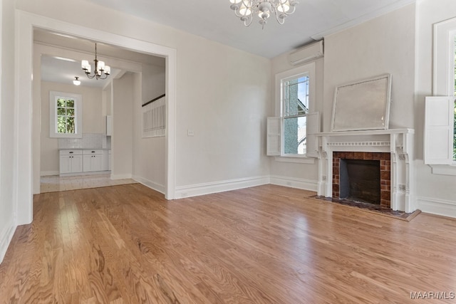 unfurnished living room with an AC wall unit, a fireplace, a chandelier, and light hardwood / wood-style flooring