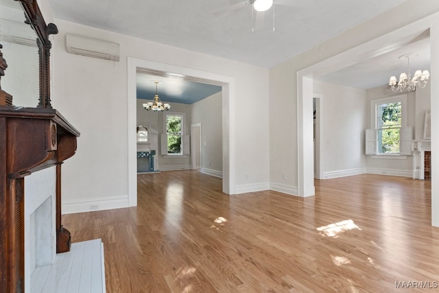 unfurnished living room featuring an AC wall unit, light hardwood / wood-style floors, and ceiling fan with notable chandelier