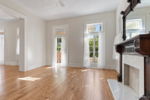 unfurnished living room with ceiling fan, light wood-type flooring, and a fireplace