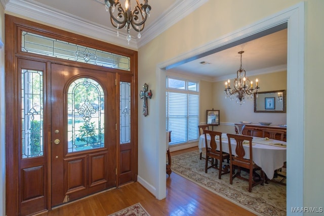 foyer entrance featuring wood-type flooring, ornamental molding, and a chandelier