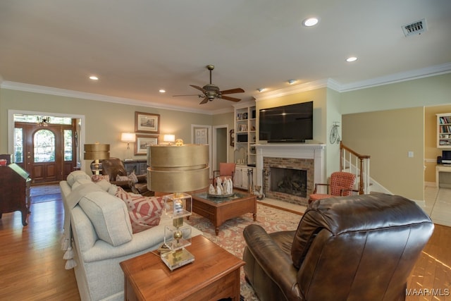 living room featuring ceiling fan, crown molding, light hardwood / wood-style flooring, and a stone fireplace