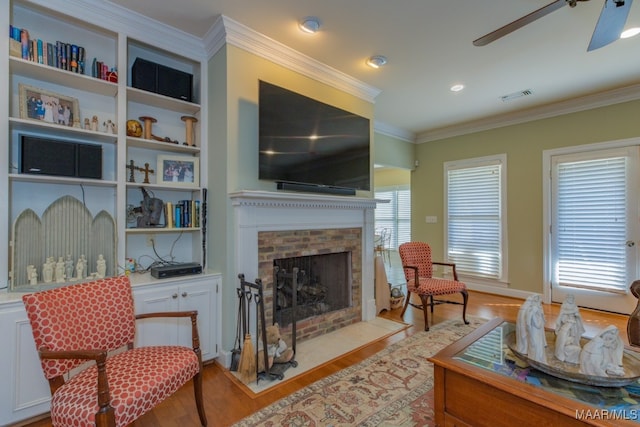 living room featuring a brick fireplace, light wood-type flooring, ornamental molding, and ceiling fan