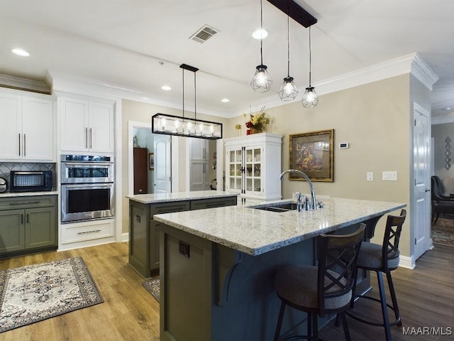 kitchen featuring white cabinetry, decorative light fixtures, a center island with sink, and stainless steel double oven