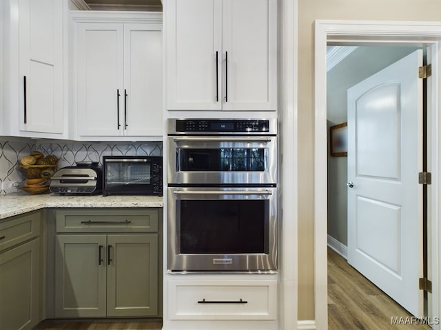 kitchen featuring decorative backsplash, white cabinets, hardwood / wood-style floors, double oven, and light stone counters