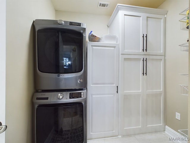 clothes washing area with cabinets, stacked washer and dryer, and light tile patterned floors