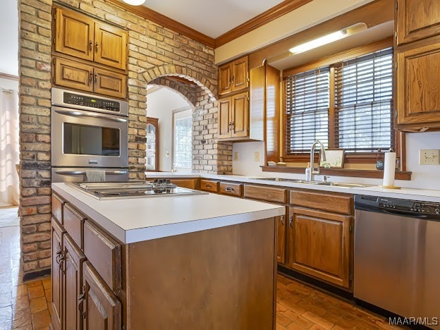 kitchen featuring a kitchen island, stainless steel dishwasher, sink, brick wall, and crown molding