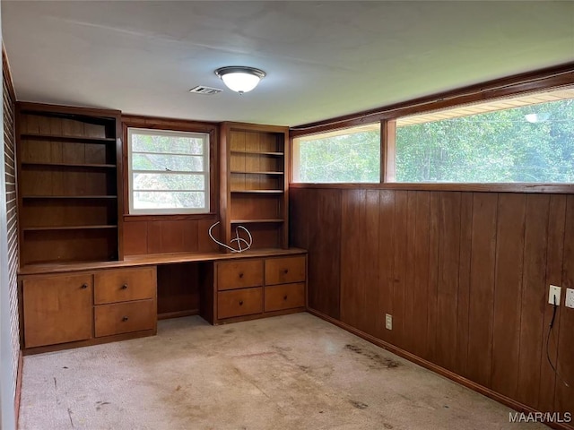 unfurnished office with light carpet, built in desk, a healthy amount of sunlight, and wood walls