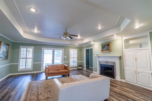 living room featuring a high end fireplace, a tray ceiling, dark wood finished floors, and baseboards