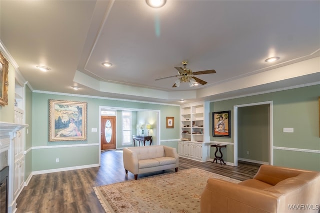 living area with baseboards, a glass covered fireplace, dark wood-type flooring, a tray ceiling, and built in shelves