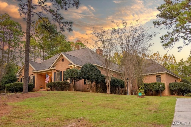 view of front of property with brick siding, a yard, and a chimney