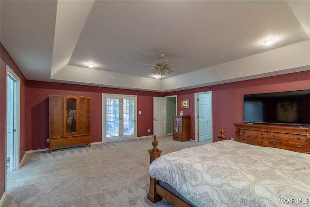 bedroom featuring a raised ceiling, light colored carpet, ceiling fan, and baseboards