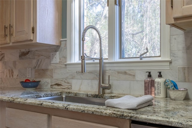 interior details featuring stainless steel dishwasher, tasteful backsplash, light stone counters, and a sink