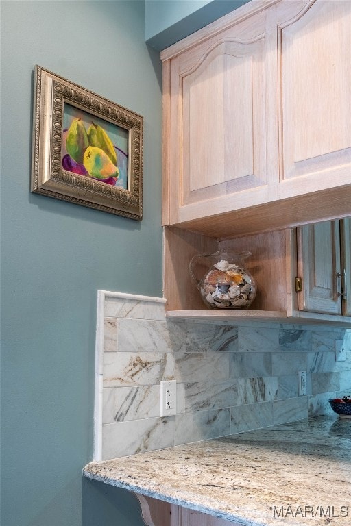 interior details with light brown cabinetry, a bar, backsplash, and light stone counters