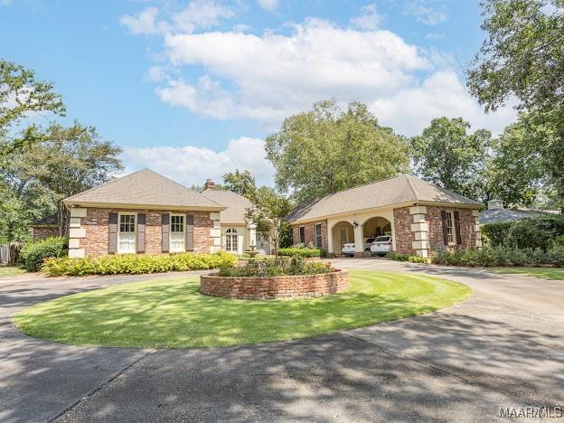 view of front facade featuring a chimney, a front lawn, and curved driveway