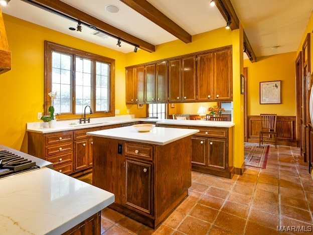 kitchen featuring tile patterned flooring, stainless steel gas cooktop, beam ceiling, sink, and a center island