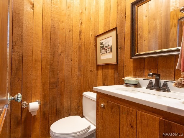 bathroom with wooden walls, vanity, and toilet