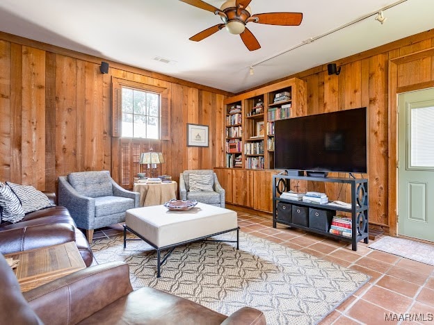 tiled living room featuring track lighting, built in shelves, wooden walls, and ceiling fan