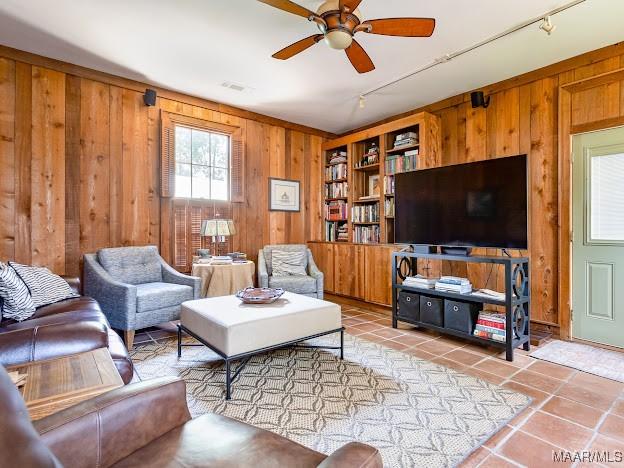 living area featuring track lighting, light tile patterned floors, ceiling fan, and wooden walls