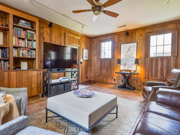 tiled living area with visible vents, ceiling fan, rail lighting, and wood walls