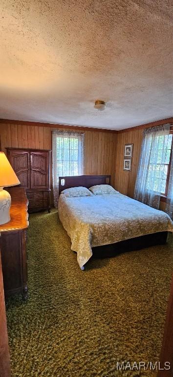 bedroom with wooden walls, a textured ceiling, and multiple windows