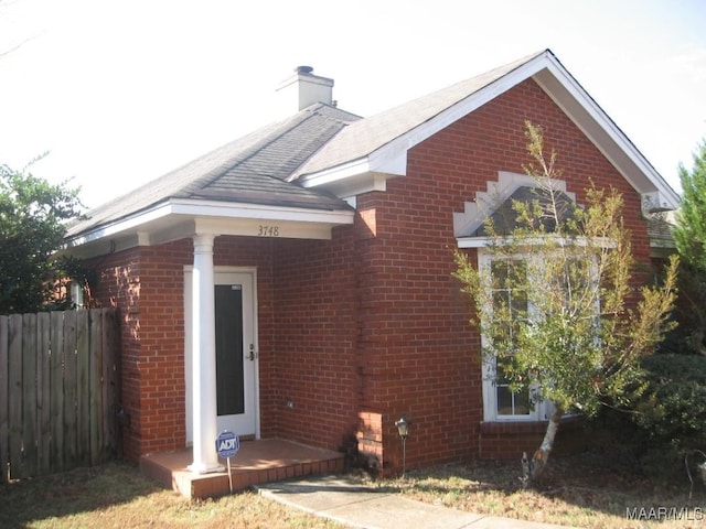 view of side of home featuring brick siding, fence, and a chimney