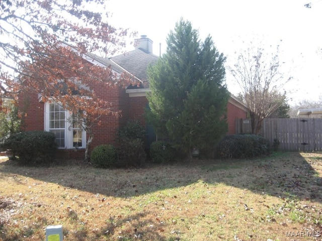 view of side of home with a yard, roof with shingles, fence, brick siding, and a chimney
