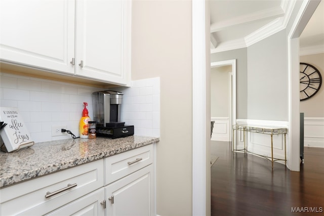 kitchen with light stone countertops, dark wood-type flooring, crown molding, white cabinetry, and backsplash