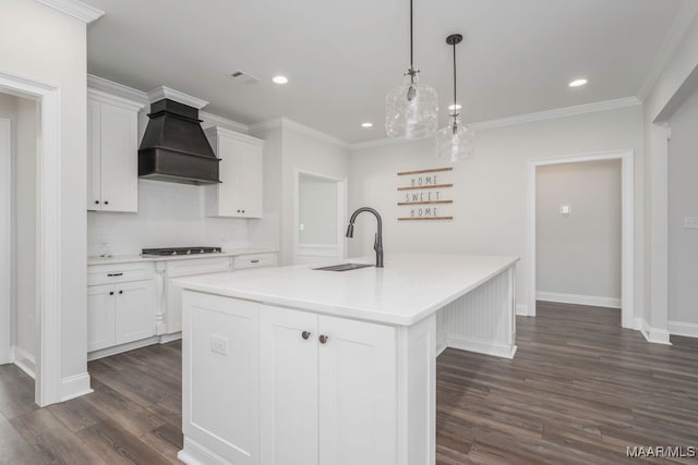 kitchen with custom range hood, white cabinets, a kitchen island with sink, and sink