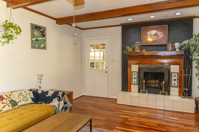 living room featuring wood-type flooring, crown molding, beam ceiling, and a tile fireplace