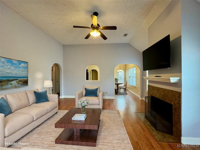 living room with a textured ceiling, light hardwood / wood-style floors, ceiling fan, and lofted ceiling