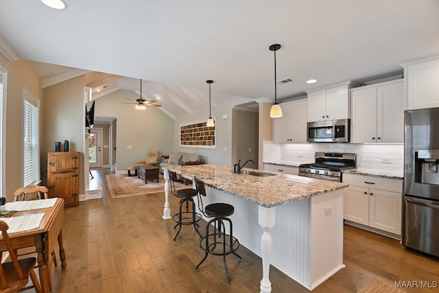 kitchen with a kitchen island with sink, vaulted ceiling with beams, hardwood / wood-style flooring, stainless steel appliances, and light stone counters