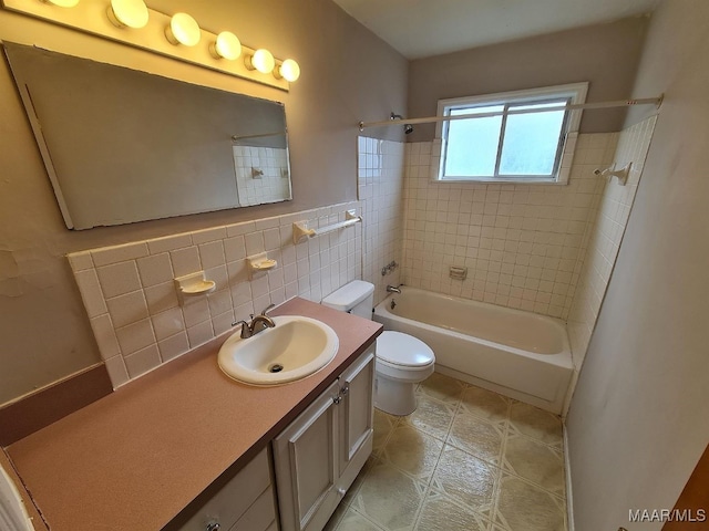 full bathroom featuring toilet, tile patterned flooring, vanity, tiled shower / bath combo, and tile walls